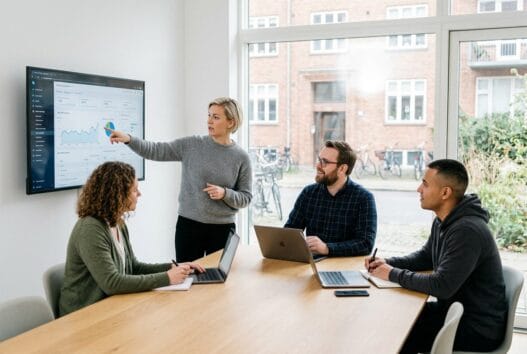 Moderne webbureau i bækkekrog med dansk team foran computer og dashboards i lyst kontormiljø