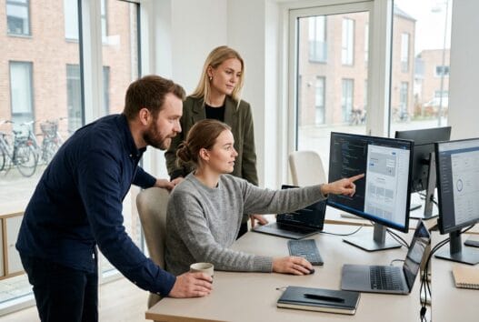 Dansk webbureau i hov med team ved computer og digitale dashboards i moderne kontormiljø