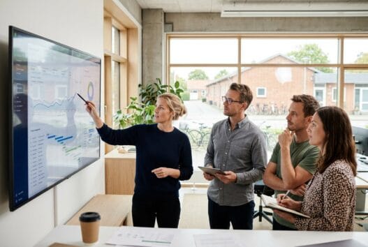 Moderne webbureau i kvistgård med team ved computere og dashboards i et lyst kontormiljø