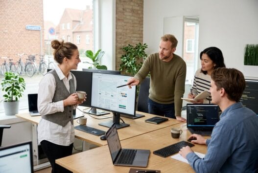 Moderne webbureau i spangsbro med team ved computer og dashboards i lyst kontormiljø
